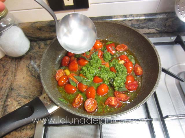aggiungi ai pomodori due cucchiai di pesto e versa un mestolo di acqua della pasta
