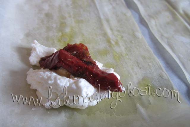 Metti una cucchiaiata di ricotta, un pomodoro secco e un pochino di sale su un lato di ogni rettangolo